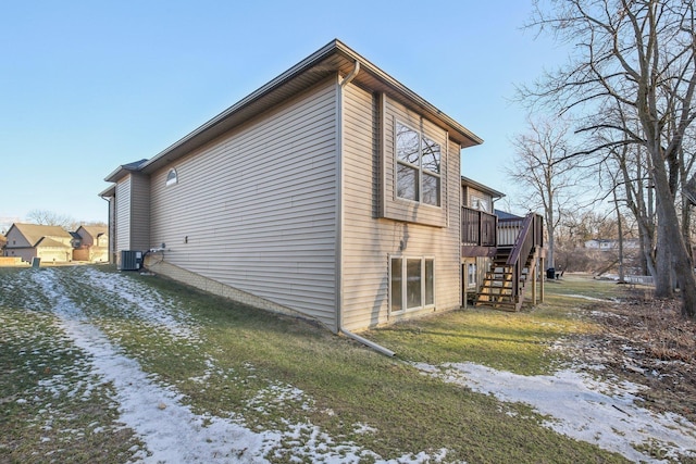 snow covered property featuring a wooden deck, central AC unit, and a lawn