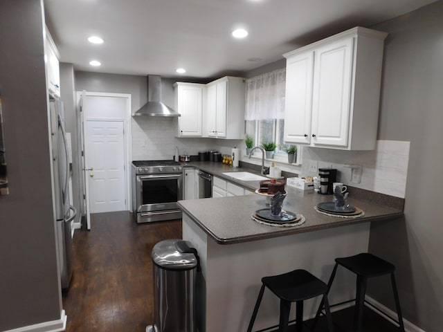 kitchen with sink, white cabinets, kitchen peninsula, stainless steel appliances, and wall chimney exhaust hood