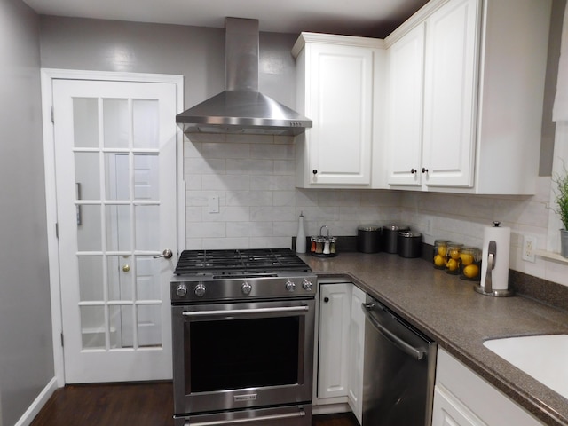 kitchen featuring appliances with stainless steel finishes, dark hardwood / wood-style floors, white cabinets, wall chimney range hood, and backsplash