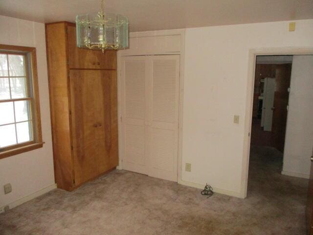 unfurnished bedroom with carpet floors, a notable chandelier, and a closet