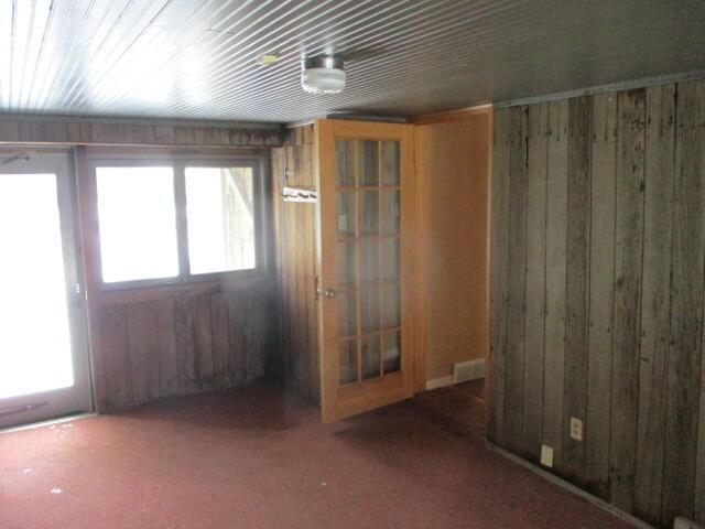 carpeted empty room featuring wood walls