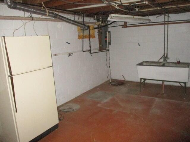 basement with white refrigerator, sink, and electric panel