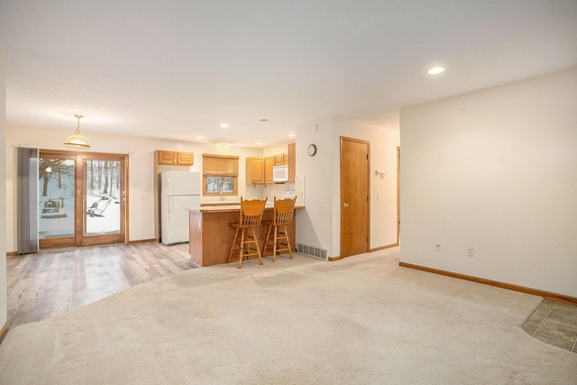 kitchen with pendant lighting, sink, white appliances, light carpet, and kitchen peninsula