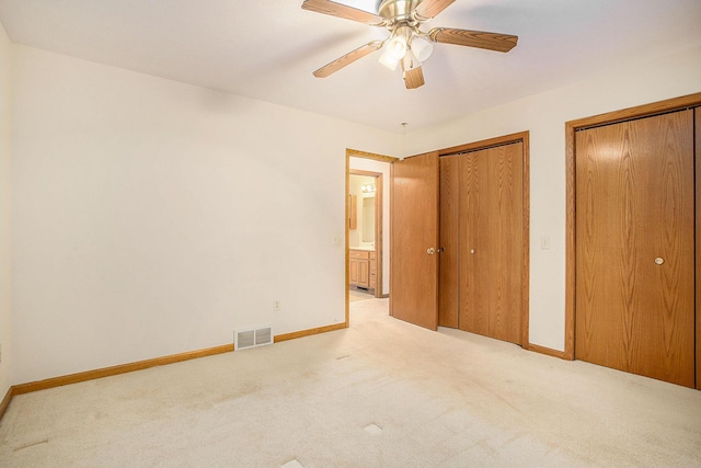 unfurnished bedroom featuring two closets, light colored carpet, and ceiling fan