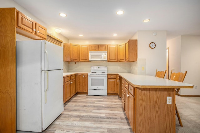 kitchen with white appliances, light hardwood / wood-style flooring, a breakfast bar area, backsplash, and kitchen peninsula