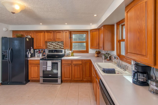 kitchen featuring appliances with stainless steel finishes, sink, backsplash, light tile patterned floors, and a textured ceiling