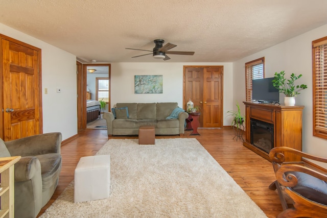 living room with ceiling fan, light hardwood / wood-style floors, and a textured ceiling