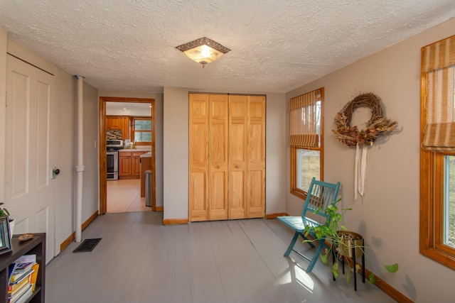 hall with a wealth of natural light, light hardwood / wood-style floors, and a textured ceiling