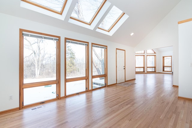 unfurnished living room with a skylight, high vaulted ceiling, and light hardwood / wood-style flooring