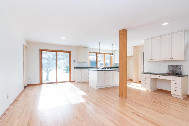 kitchen with white cabinetry, built in desk, pendant lighting, and light wood-type flooring