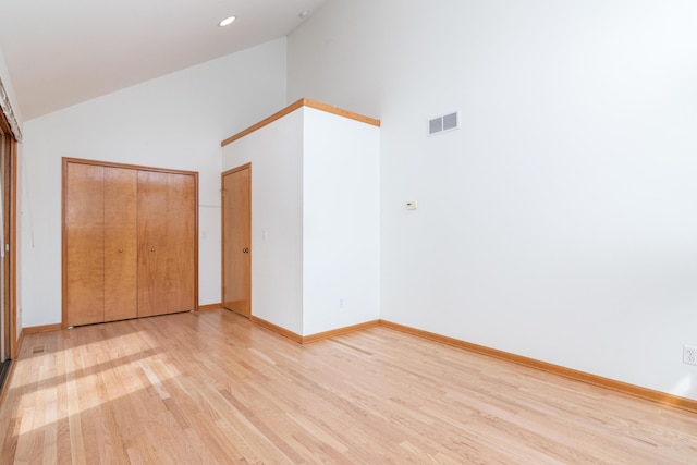 unfurnished bedroom featuring high vaulted ceiling, light hardwood / wood-style floors, and a closet