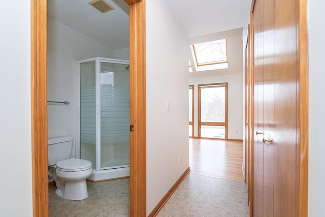 bathroom with walk in shower, toilet, and a skylight