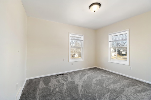 spare room featuring plenty of natural light and dark colored carpet