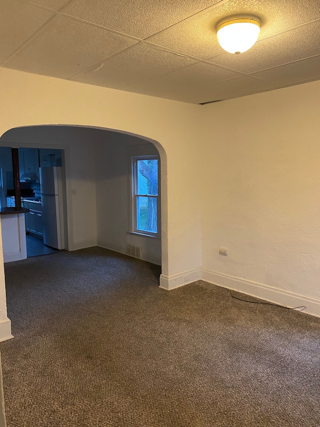 spare room with a paneled ceiling and dark colored carpet