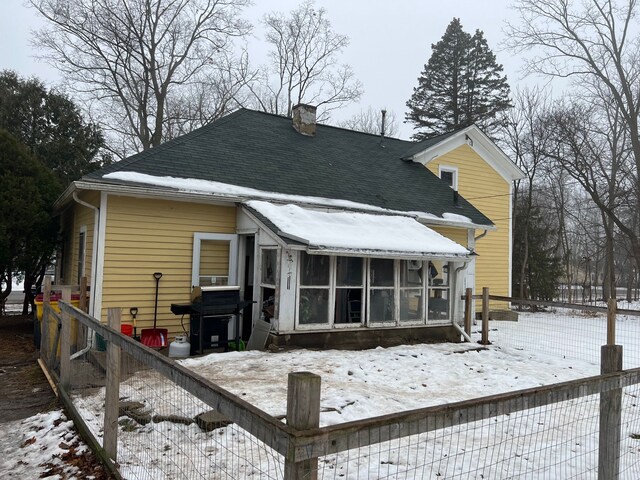 snow covered rear of property featuring a sunroom