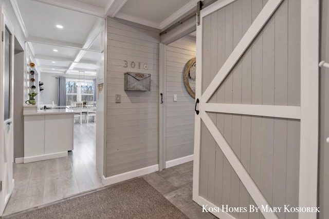 corridor featuring a barn door, coffered ceiling, beam ceiling, and wood walls