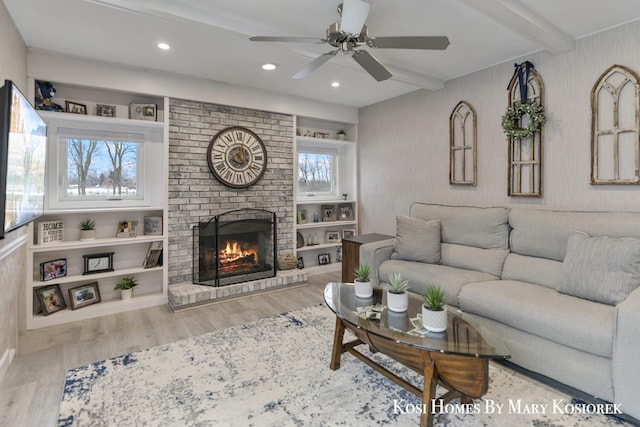 living room featuring ceiling fan, beam ceiling, hardwood / wood-style floors, and a brick fireplace