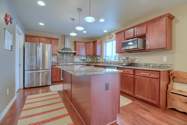 kitchen with sink, a kitchen island, pendant lighting, stainless steel appliances, and wall chimney range hood