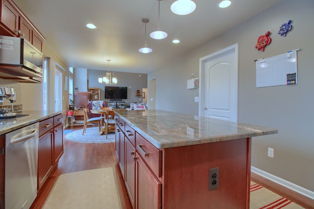 kitchen featuring stainless steel dishwasher, decorative light fixtures, light stone countertops, and a kitchen island