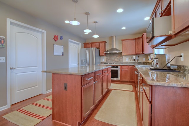 kitchen with pendant lighting, wall chimney range hood, sink, stainless steel appliances, and a center island