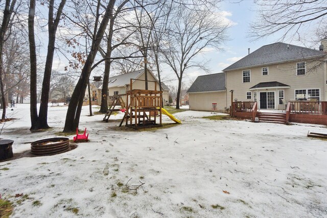 yard layered in snow with a playground, a wooden deck, and a fire pit