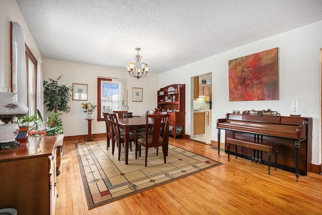 dining space with wood-type flooring, a notable chandelier, and a textured ceiling