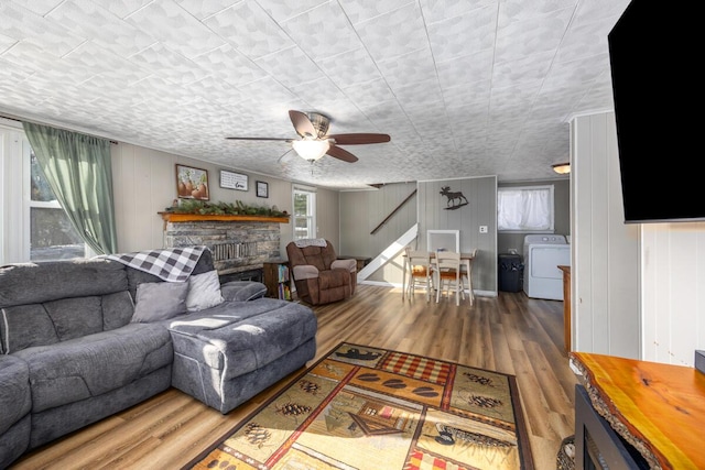 living room with washer / clothes dryer, wood-type flooring, a stone fireplace, and ceiling fan