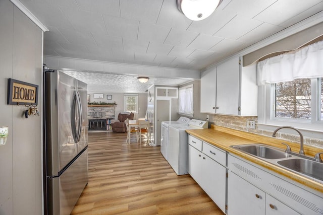 kitchen featuring sink, washer and dryer, stainless steel fridge, light hardwood / wood-style floors, and white cabinets