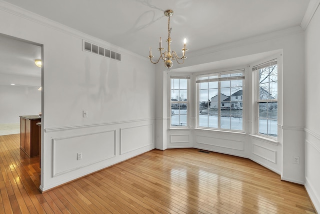 unfurnished dining area featuring an inviting chandelier, crown molding, and light wood-type flooring