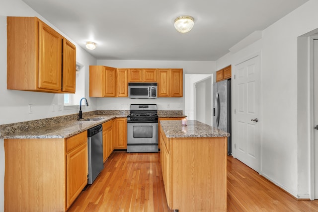 kitchen with stone countertops, sink, a center island, stainless steel appliances, and light hardwood / wood-style flooring