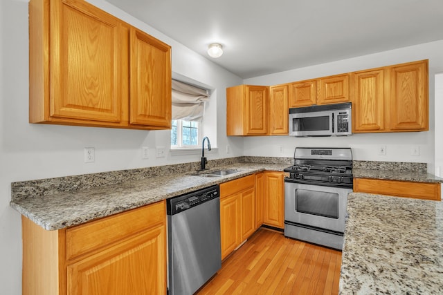 kitchen featuring light stone countertops, appliances with stainless steel finishes, sink, and light wood-type flooring