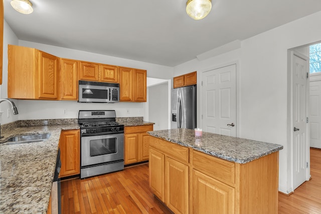 kitchen featuring stainless steel appliances, a center island, sink, and light stone counters