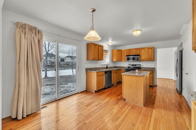 kitchen with sink, stainless steel appliances, a kitchen island, decorative light fixtures, and light wood-type flooring