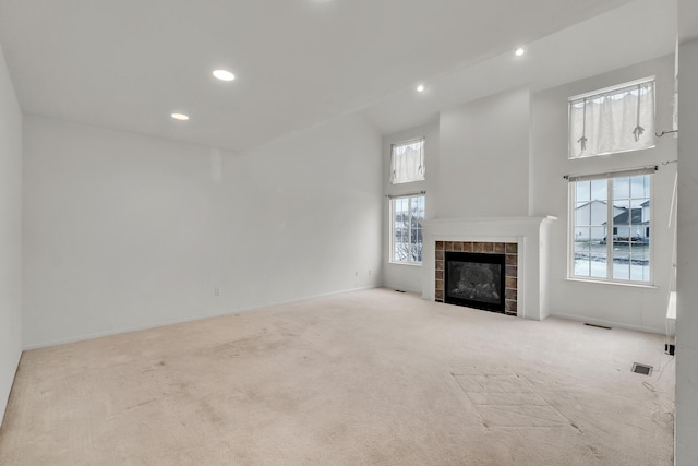 unfurnished living room featuring a high ceiling, a tile fireplace, and light colored carpet