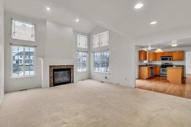 unfurnished living room with a tile fireplace, a wealth of natural light, light colored carpet, and high vaulted ceiling