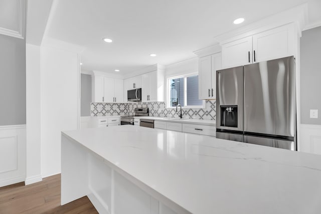 kitchen with light stone counters, appliances with stainless steel finishes, hardwood / wood-style floors, and white cabinets