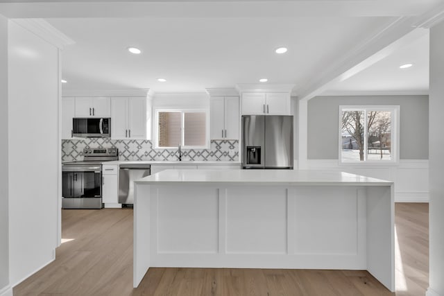 kitchen with appliances with stainless steel finishes, sink, backsplash, white cabinets, and light wood-type flooring