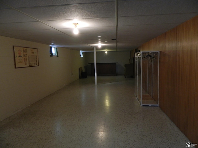 basement featuring a drop ceiling and wood walls