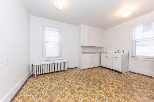 interior space featuring sink, radiator heating unit, and white cabinets