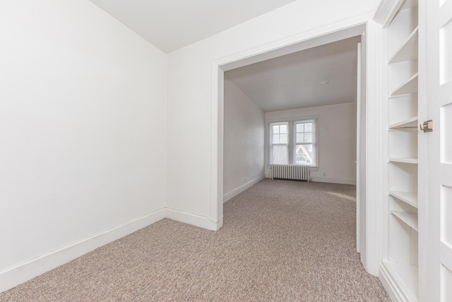 empty room featuring radiator heating unit, light colored carpet, and built in shelves