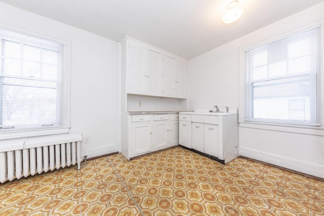 kitchen with sink, radiator heating unit, and white cabinets