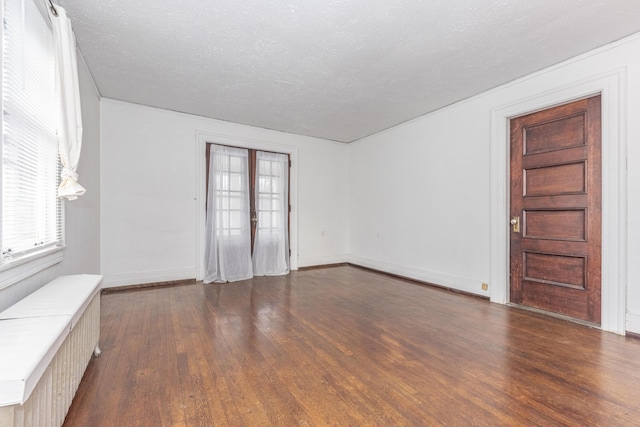 empty room featuring radiator, dark wood-type flooring, french doors, and a textured ceiling