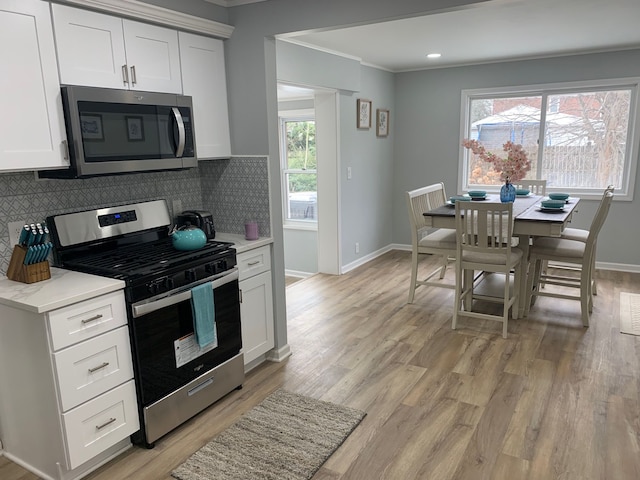 kitchen featuring appliances with stainless steel finishes, tasteful backsplash, ornamental molding, light hardwood / wood-style floors, and white cabinets