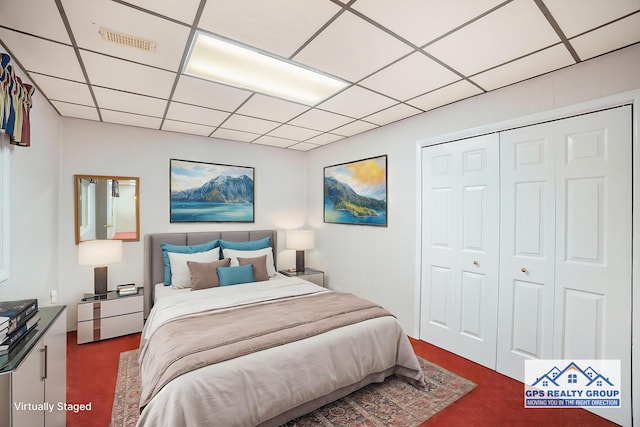 bedroom featuring dark colored carpet, a paneled ceiling, and a closet