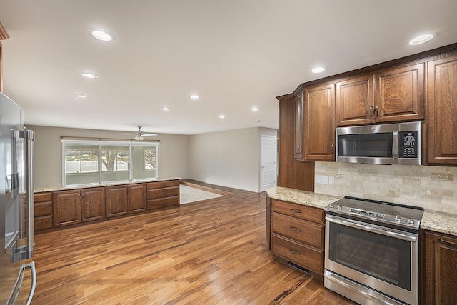 kitchen featuring stainless steel appliances, light stone counters, backsplash, and light wood-type flooring