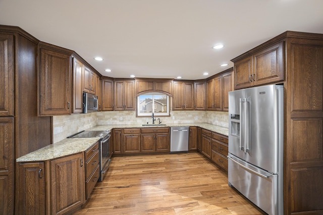 kitchen with tasteful backsplash, sink, light stone counters, light hardwood / wood-style floors, and stainless steel appliances