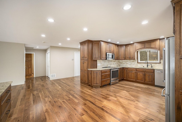 kitchen with sink, appliances with stainless steel finishes, light hardwood / wood-style floors, light stone countertops, and decorative backsplash