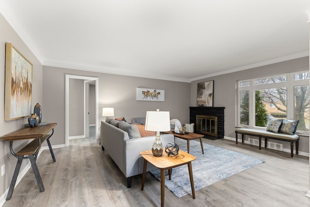 living room with a brick fireplace, crown molding, and light hardwood / wood-style flooring