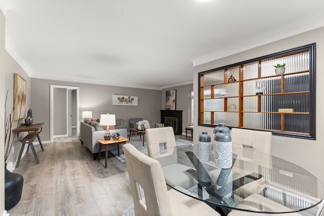 dining room featuring a fireplace, crown molding, and light hardwood / wood-style flooring