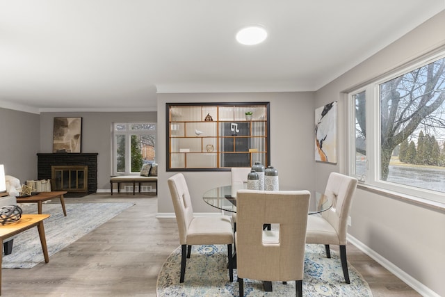 dining area featuring ornamental molding, wood-type flooring, and a brick fireplace